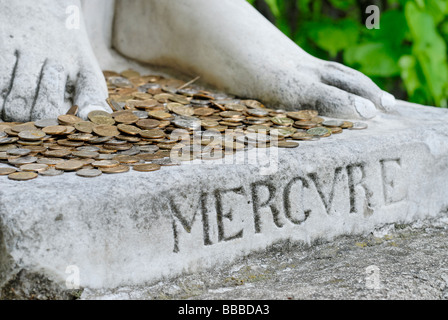 Monete metalliche in corrispondenza dei piedi di Dio statua di Mercurio Foto Stock