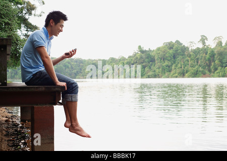 Uomo cinese seduto sul molo, guardando il telefono cellulare Foto Stock