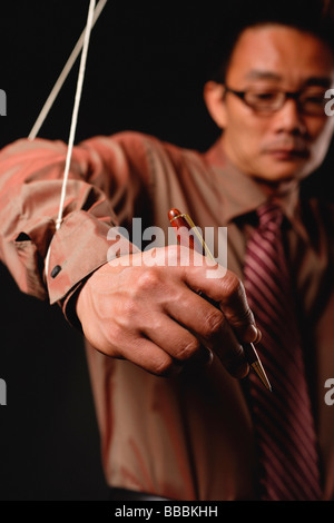 Uomo con marionette stringhe allegate alle sue mani, tenendo pen Foto Stock