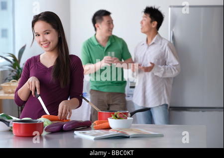 La donna la cottura mentre gli uomini parlare Foto Stock