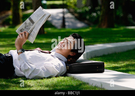 Un uomo si trova verso il basso e leggere il giornale nel parco Foto Stock