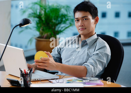 Un uomo guarda la telecamera come egli siede alla sua scrivania Foto Stock