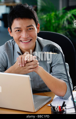 Un uomo sorride alla telecamera come egli siede alla sua scrivania Foto Stock