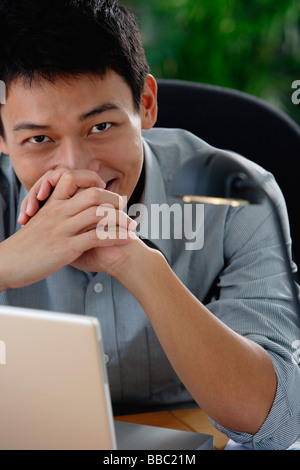 Un uomo sorride alla telecamera come egli siede alla sua scrivania Foto Stock