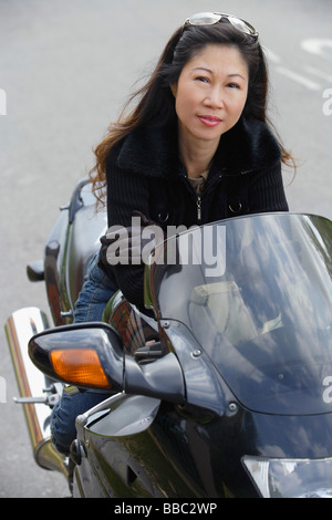 Donna matura seduto sul motociclo, sorridente in telecamera Foto Stock