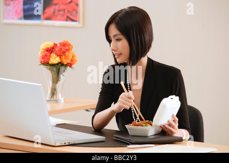 Una donna mangia il pranzo alla sua scrivania mentre si lavora Foto Stock