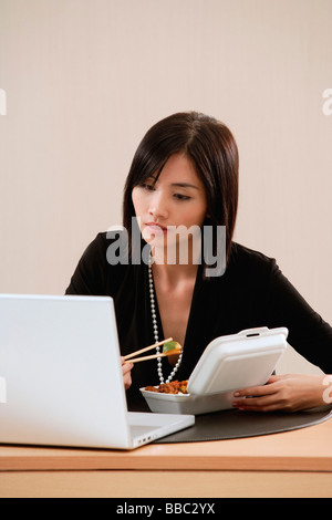 Una donna mangia il pranzo alla sua scrivania mentre si lavora Foto Stock