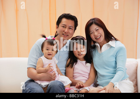 Ritratto di famiglia di 4, mamma, papà e due figlie, seduto sul lettino, sorridente, guardando la fotocamera Foto Stock