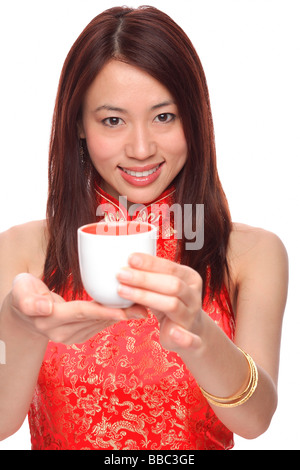 Giovane donna indossa cheongsam, tenendo il tè verso la telecamera Foto Stock