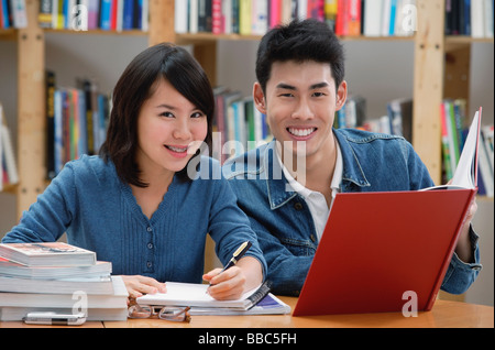 Giovane studiare in biblioteca, sorridente in telecamera Foto Stock