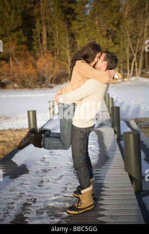 Man picking up donna su terreni innevati pier Foto Stock