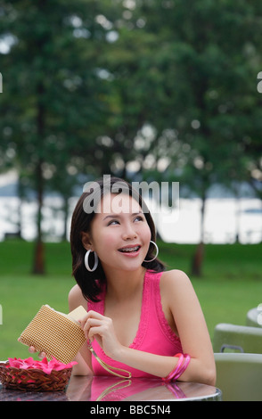 Giovane donna seduta al tavolo esterno, tenendo wallet, guardando lontano Foto Stock