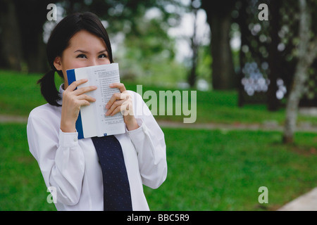 Giovane donna in uniforme scolastica, libro che ricopre la faccia Foto Stock