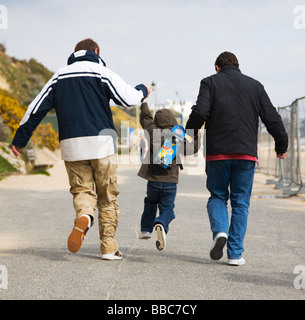 Tre generazioni di una famiglia. Un giovane ragazzo salta tra il suo papà e il nonno. Fronte mare di Bournemouth. Il Dorset. Regno Unito. Foto Stock