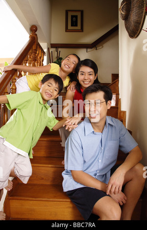 Famiglia con due bambini seduti sulle scale, sorridente in telecamera Foto Stock