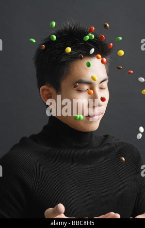Giovane uomo vestito di nero, gettando multi caramelle colorate in aria Foto Stock