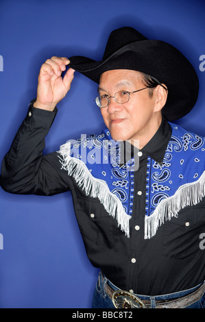 Senior uomo vestito in costumi da cowboy, regolazione hat Foto Stock