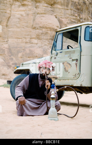 Un uomo beduino di fumare un waterpipe (shisha o narghile) nel Wadi Rum desert, Giordania. Foto Stock