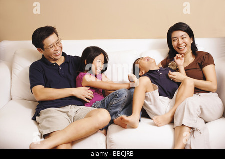Famiglia di quattro sul divano, sorella solletico fratello Foto Stock