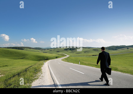 Imprenditore a piedi lungo un paese isolato su strada vista posteriore Foto Stock