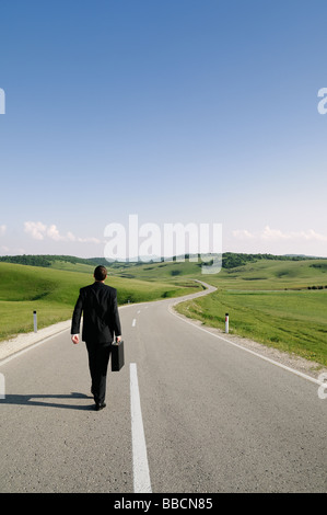 Imprenditore a piedi lungo un paese isolato su strada vista posteriore Foto Stock