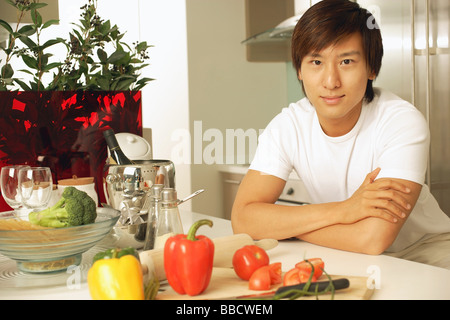 Giovane uomo appoggiata sul banco di cucina, con le braccia incrociate Foto Stock