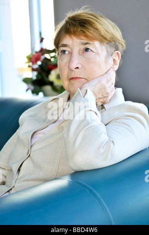 Triste anziani donna seduta su un divano in ambienti interni Foto Stock