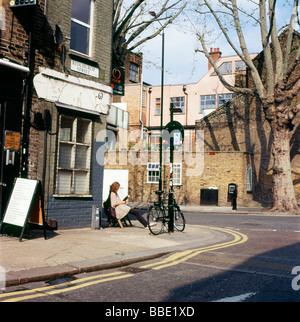 Una donna seduta al di fuori di un negozio all'angolo di Redchurch Street e Club Row in Shoreditch East London REGNO UNITO KATHY DEWITT Foto Stock