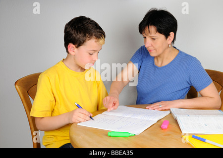 Ragazzo facendo i compiti per la scuola, madre aiutandolo Foto Stock