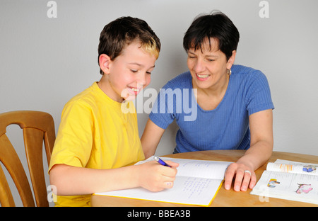 Ragazzo facendo i compiti per la scuola, madre aiutandolo, entrambi a ridere Foto Stock