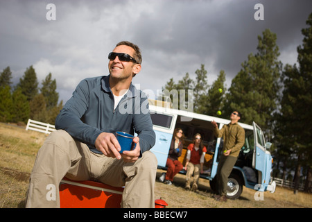 Gruppo di amici per un viaggio di campeggio, uomo seduto su un raffreddatore di bere caffè, piegare, Oregon, Stati Uniti d'America Foto Stock