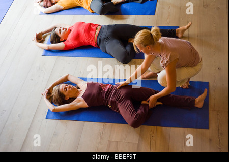 Le donne nella classe di yoga facendo la posizione dell'albero con l'aiuto dell'istruttore Foto Stock