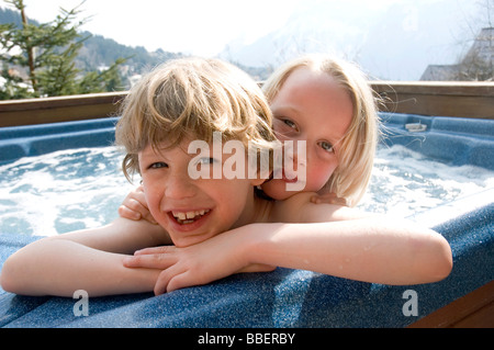 Due bambini godono di una porta fuori la vasca calda a loro chalet dopo lo sci nelle Alpi francesi Foto Stock