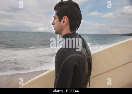 Giovane uomo in wetsuit tenendo la sua tavola da surf Foto Stock