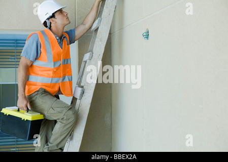 L'uomo salendo la scala che porta cassetta degli attrezzi Foto Stock