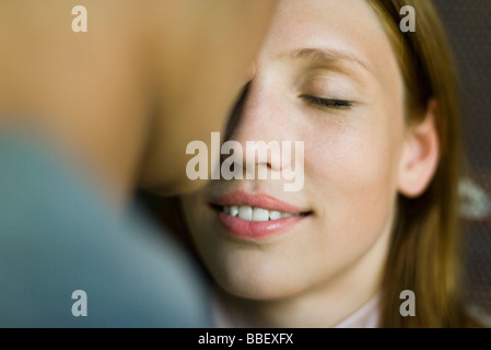 Giovane donna sorridente come uomo bacia la fronte, gli occhi chiusi Foto Stock