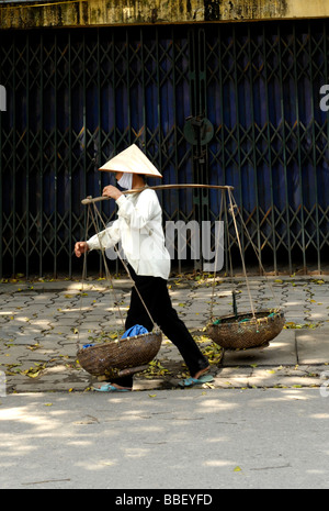 Signora vietnamita indossando il tradizionale trasporto conehat stick con due cestelli di bambù, Hanoi, Vietnam. Foto Stock