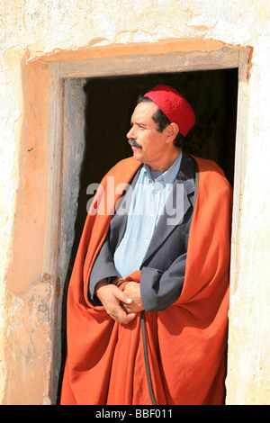 Uomo con i baffi indossando un tradizionale djellaba e red fez in Tataouine, Tunisia Foto Stock
