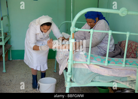 Una suora che lavora come infermiera in una colonia di lebbra è il trattamento di un lebbroso che ha dolorose ferite ai suoi piedi. Foto Stock