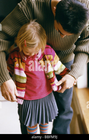 Padre di piegarsi per aiutare i giovani figlia cardigan pulsante Foto Stock