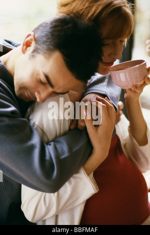 L'uomo abbracciando moglie incinta, donna bere il tè Foto Stock