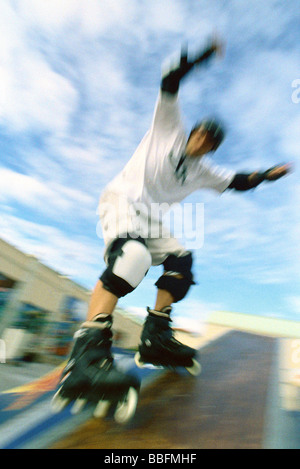 Skater inline a braccia alzate con scorrimento sulla rampa di skatepark Foto Stock