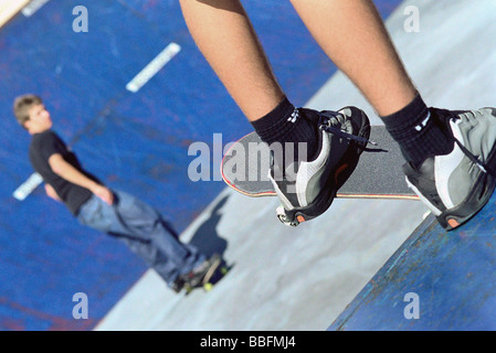 Guidatore di skateboard appollaiato sul bordo della rampa guardando amico skate su rampa inferiore Foto Stock