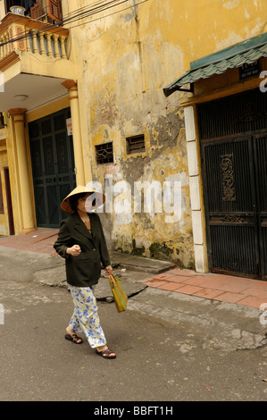 Il vietnamita old Lady indossando il tradizionale conehat passeggiando nel quartiere vecchio, Hanoi, Vietnam. Foto Stock