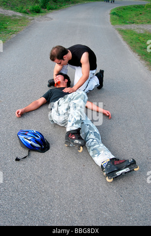 Primo soccorso, in-line skater sul pavimento dopo caduta, immobile, persona aiutando Foto Stock