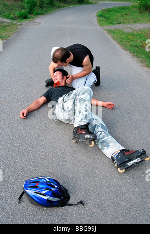 Primo soccorso, in-line skater sul pavimento dopo caduta, immobile, persona aiutando Foto Stock