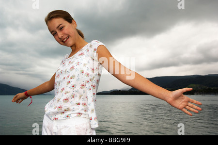 Ragazza giovane allarga le braccia davanti a un lago Foto Stock