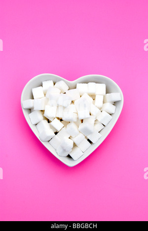 Cuore bianco a forma di ciotola riempita con cubetti di zucchero in rosa Foto Stock