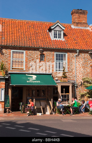 I clienti seduti fuori nel sole bere il tè e caffè a Byfords delicatessen restaurant cafe in Holt Norfolk Regno Unito Foto Stock