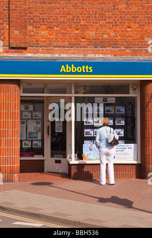 Una donna che guarda nella finestra degli Abati agenti immobiliari finestra al case in vendita nella città di Holt Norfolk Regno Unito Foto Stock